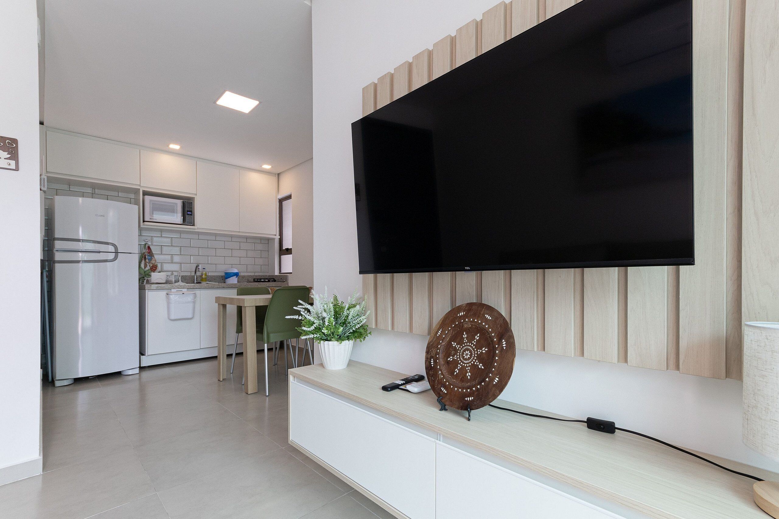 A modern kitchen with a built-in microwave, a dining area with a green chair, and a large flat-screen TV mounted on the wall.