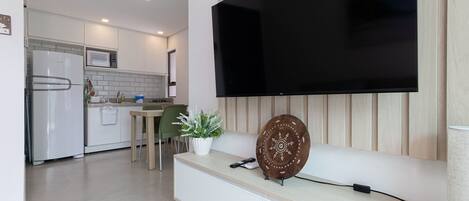 A modern kitchen with a built-in microwave, a dining area with a green chair, and a large flat-screen TV mounted on the wall.