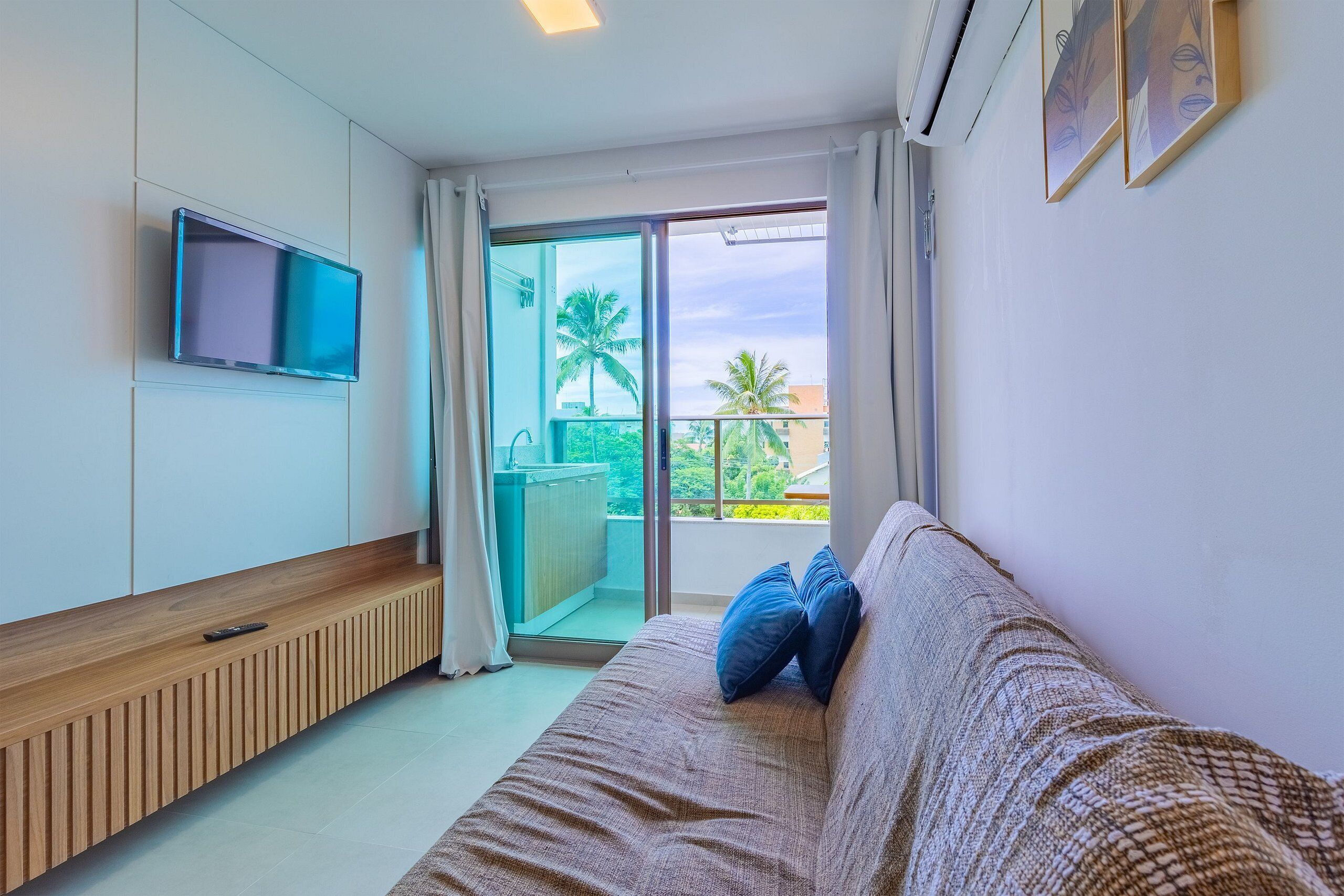 Un soggiorno moderno con un divano, una TV a parete e una porta scorrevole in vetro che dà su un balcone con vista su palme.