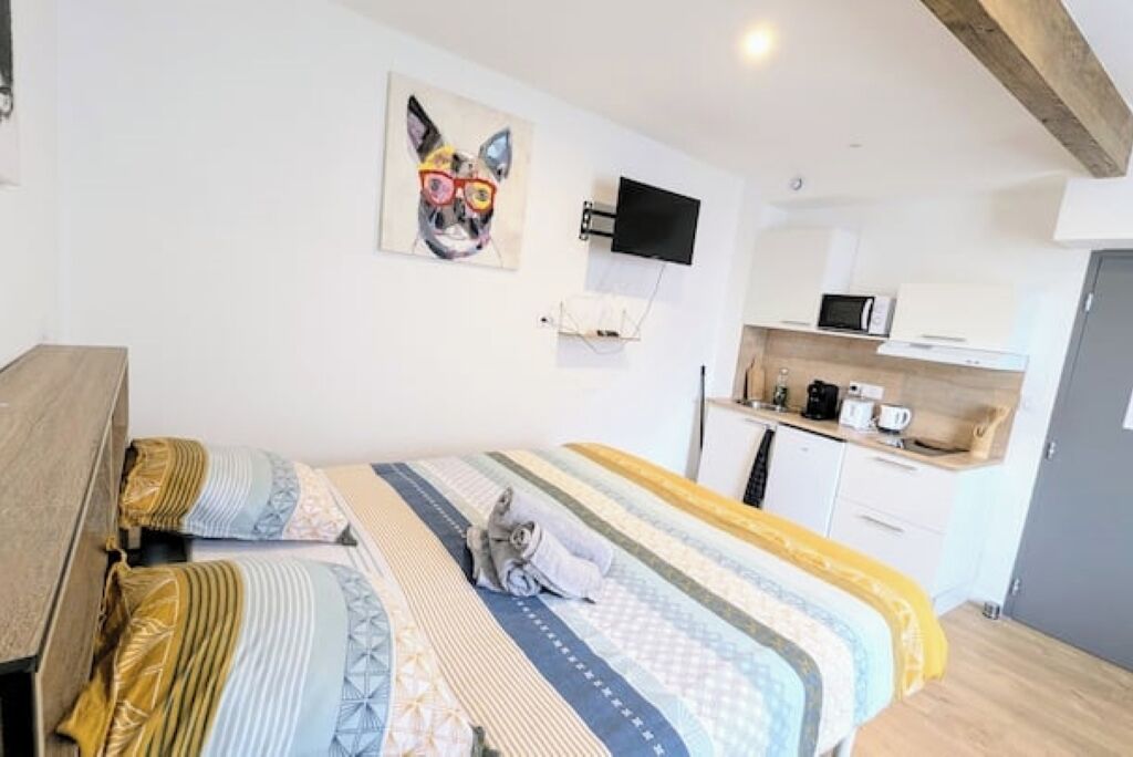 A bedroom with a bed, a TV mounted on the wall, and a kitchenette area with a microwave and coffee maker.
