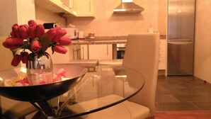 A modern kitchen with a glass dining table, a vase with red flowers, and stainless steel appliances. - Modern apartment on the Fisterra Road (Negreira)