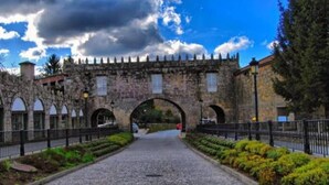 A cobblestone pathway leading to a historic stone gate with arched openings, flanked by a metal fence and greenery. - Modern apartment on the Fisterra Road (Negreira)