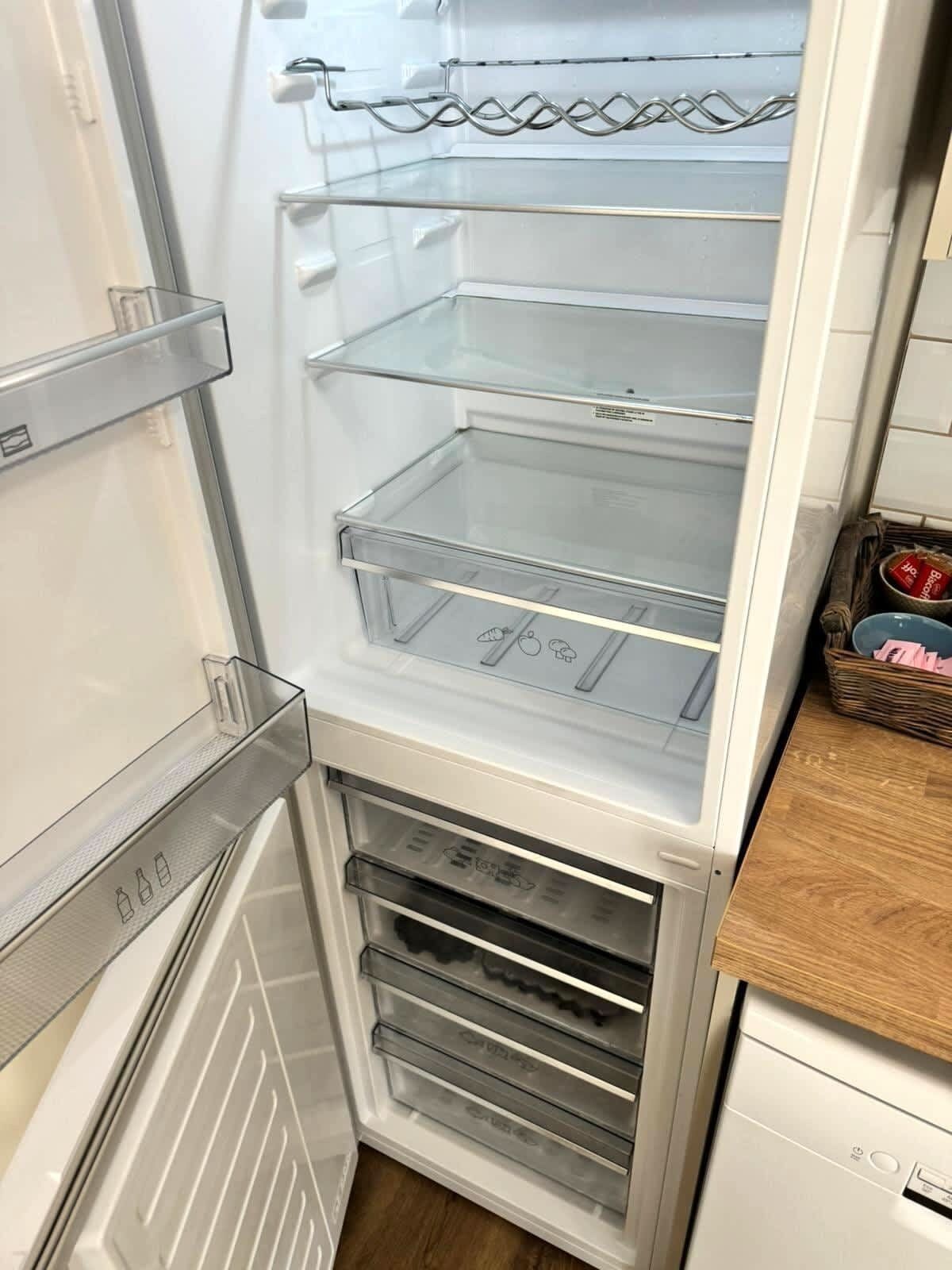 Un réfrigérateur ouvert, doté de plusieurs étagères et de tiroirs, dont une étagère en verre et une grille métallique.