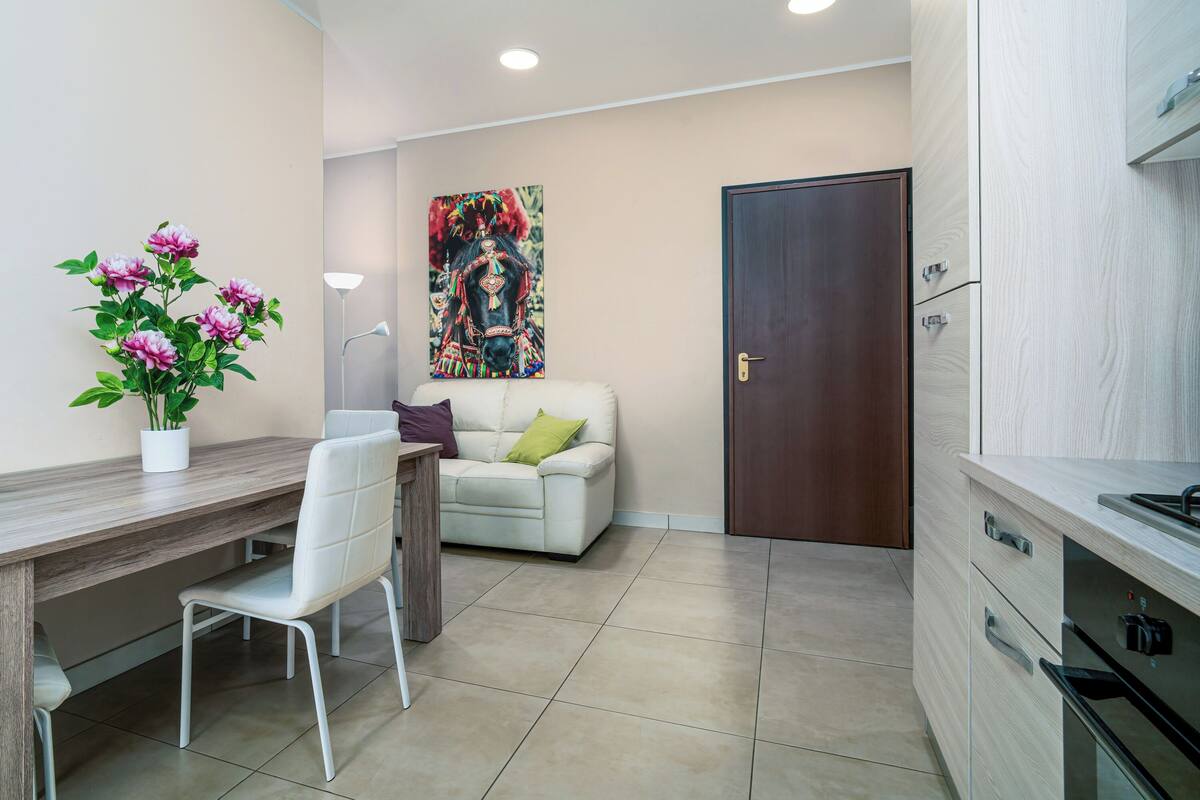 A modern kitchen with a wooden countertop, a white chair, a sofa with cushions, and a door in the background.