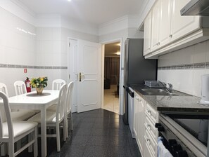 A kitchen with white cabinets, a granite countertop, and a dining area with white chairs and a table. - Sea View Forum Wi-Fi, AC & Parking 1 minute from Forum Madeira (Funchal)
