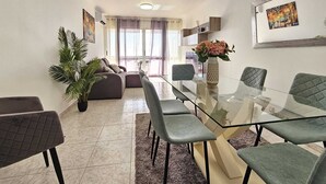 A modern living room with a glass dining table, grey upholstered chairs, a sofa, and a potted plant. - Sea View Forum Wi-Fi, AC & Parking 1 minute from Forum Madeira (Funchal)