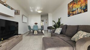 A modern living room with a grey sofa, a TV, and a dining area with a table and chairs. - Sea View Forum Wi-Fi, AC & Parking 1 minute from Forum Madeira (Funchal)