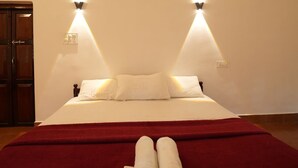 A hotel room with a bed, two wall-mounted lights, a ceiling fan, and a red bedspread.