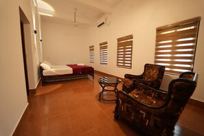 A hotel room with a bed, a chair, a small table, and a ceiling fan. - Chandralayam Homesay  (Bekal)