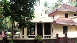 A two-story house with a tiled roof, a balcony with a railing, and a gated entrance.