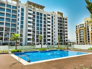 A modern building with a swimming pool, surrounded by greenery and palm trees.