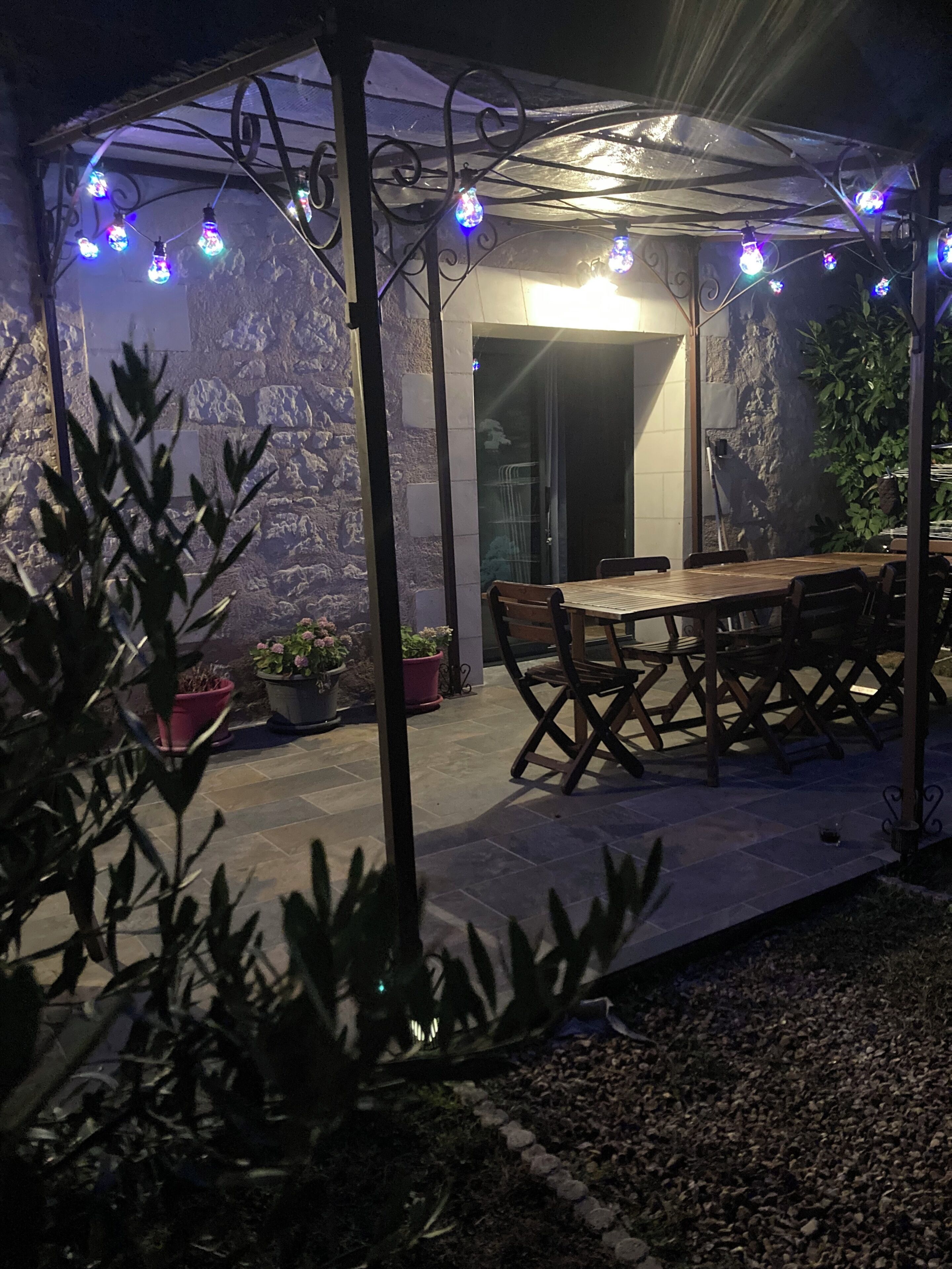 An outdoor patio area with a wooden table and chairs, surrounded by potted plants and stone walls.