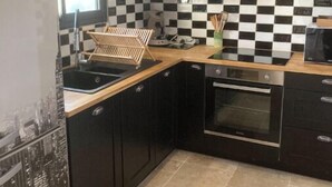 A compact kitchen with black cabinets, a checkered backsplash, a built-in oven, and a window providing natural light.
