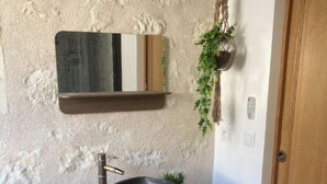 A bathroom with a stone sink on a wooden stand, a mirror above it, and a hanging plant.