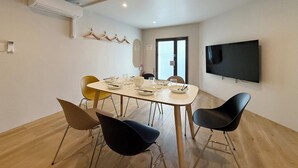 Un comedor moderno con una mesa redonda, sillas negras y amarillas, un televisor montado y un equipo de aire acondicionado.