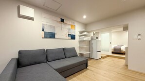 Una sala de estar moderna con un sofá seccional gris, un televisor blanco montado en la pared, un refrigerador blanco y piso de madera.