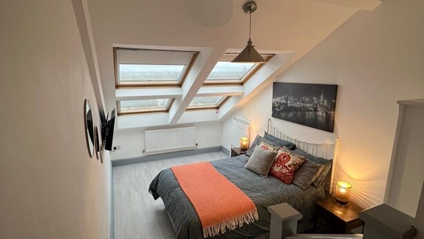 A bedroom with skylights, a bed with a blanket, a nightstand with a lamp, and a cityscape painting on the wall. - The Penthouse Loft with Skyline views (Northampton)