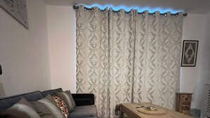 A living room with a dark-colored sofa, a wooden coffee table, patterned curtains, and a small wooden cabinet. - The Penthouse Loft with Skyline views (Northampton)