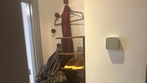 A hallway with a coat rack holding various coats and a fur-lined jacket. A shoe rack with multiple pairs of shoes is also visible. - The Penthouse Loft with Skyline views (Northampton)