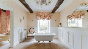 A classic bathroom with a freestanding bathtub, wooden flooring, and floral-patterned curtains. - Ormesby Manor - 8 Beds - Sleeps 16 - Hot Tub (Great Yarmouth)
