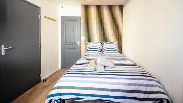 A room with a bed, a wooden ceiling beam, a striped headboard, and a door. - Studio 3 - Cocon Douillet : Le Confort  (Gond-Pontouvre)