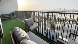 A balcony with a sofa and a chair, a small table, and a view of a cityscape with palm trees and a body of water. - Easygo-upgraded 1bdr Mageye MBR (Dubai)