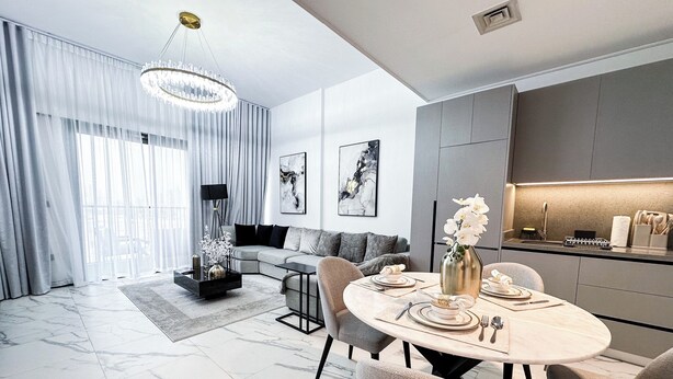 A modern living room with a dining area, featuring a marble floor, a round dining table with chairs, a sofa, and a kitchen area with a countertop and cabinets. - Easygo-upgraded 1bdr Mageye MBR (Dubai)