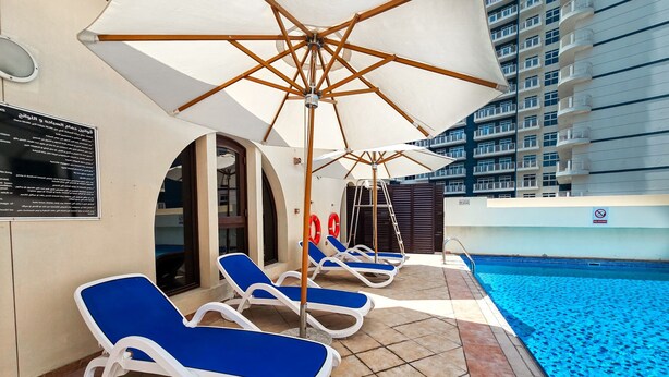 A poolside area with lounge chairs and umbrellas, a pool, and a high-rise building in the background. - Easygo- Spaciou STU With Pool Viewlp17 (Dubai)