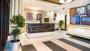A hotel lobby with a reception desk, potted plants, framed artwork on the walls, and a staircase leading to other areas. - Easygo- Spaciou STU With Pool Viewlp17 (Dubai)