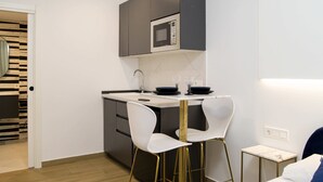 Una cocina moderna con microondas integrado, dos taburetes blancos tipo barra y una pequeña mesa blanca.