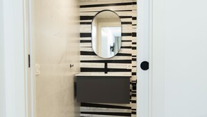 Un baño con pared a rayas negras y blancas, un espejo redondo y un lavamanos oscuro.