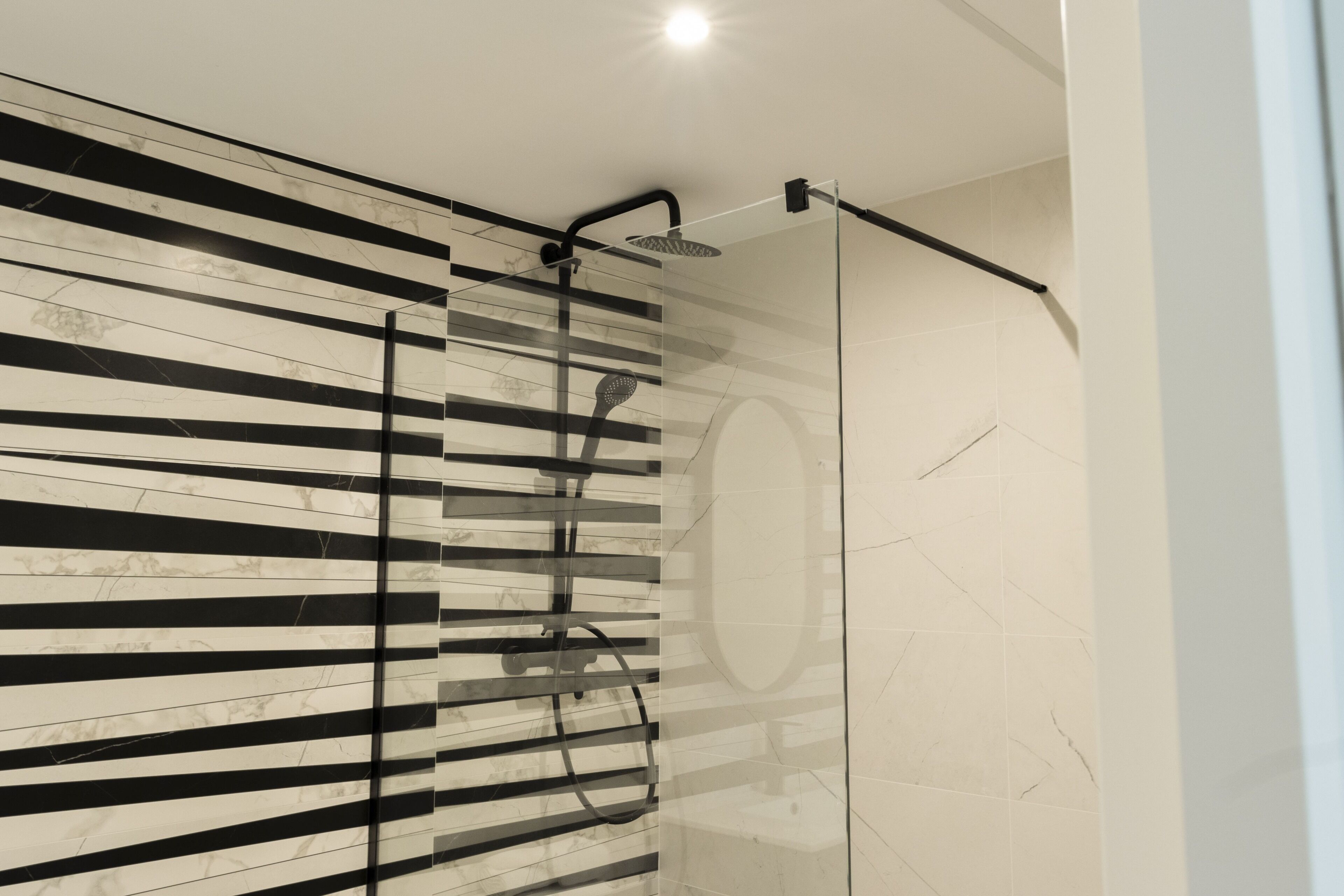 Un baño moderno con cabina de ducha de vidrio, pared a rayas negras y blancas y suelo de mármol.