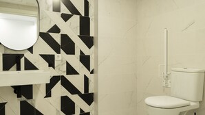 A bathroom with a white toilet, a mirror above the sink, and a geometric black and white tile backsplash. - Forata Lofts, Room 3 (Valencia)