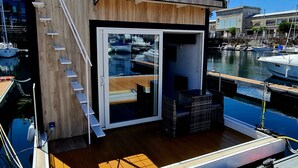 A modern boat with a wooden deck, a glass door leading to an interior space, and a metal railing on the upper deck. - Floating apartment in the nautical Vigo ferry dock Cies Islands and Cangas (Vigo)