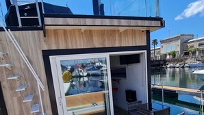 A modern boat with a wooden deck, a glass door leading to a covered area, and a view of boats in the marina. - Floating apartment in the nautical Vigo ferry dock Cies Islands and Cangas (Vigo)