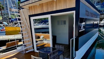 A modern boat with a wooden deck, glass railings, and a small seating area.