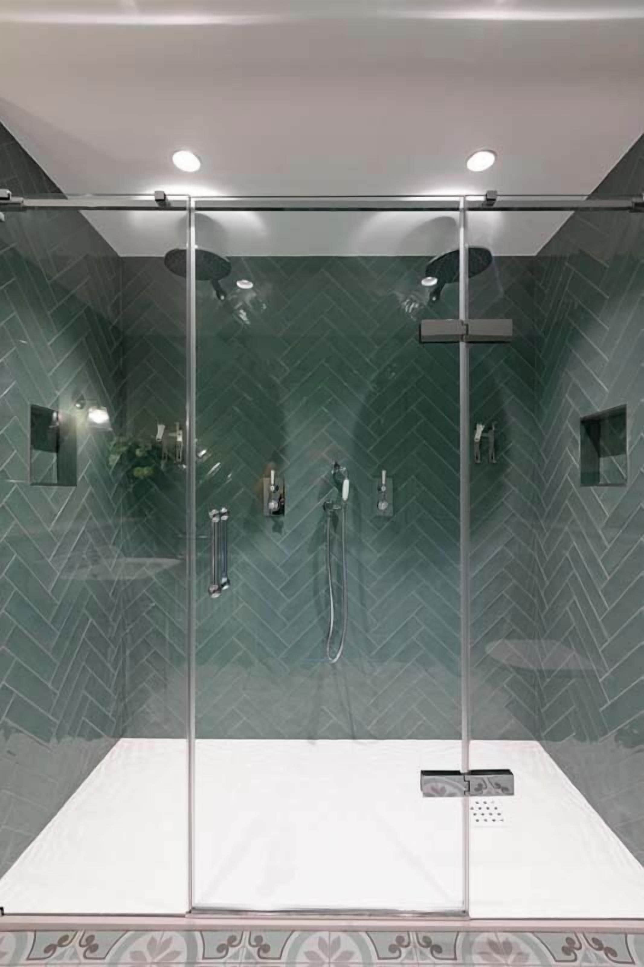 A modern shower with a glass enclosure, a control panel, and a herringbone-patterned wall.