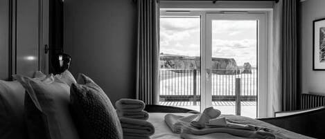 A hotel room with a bed, a side table, a window with curtains, and a view of the outdoors.