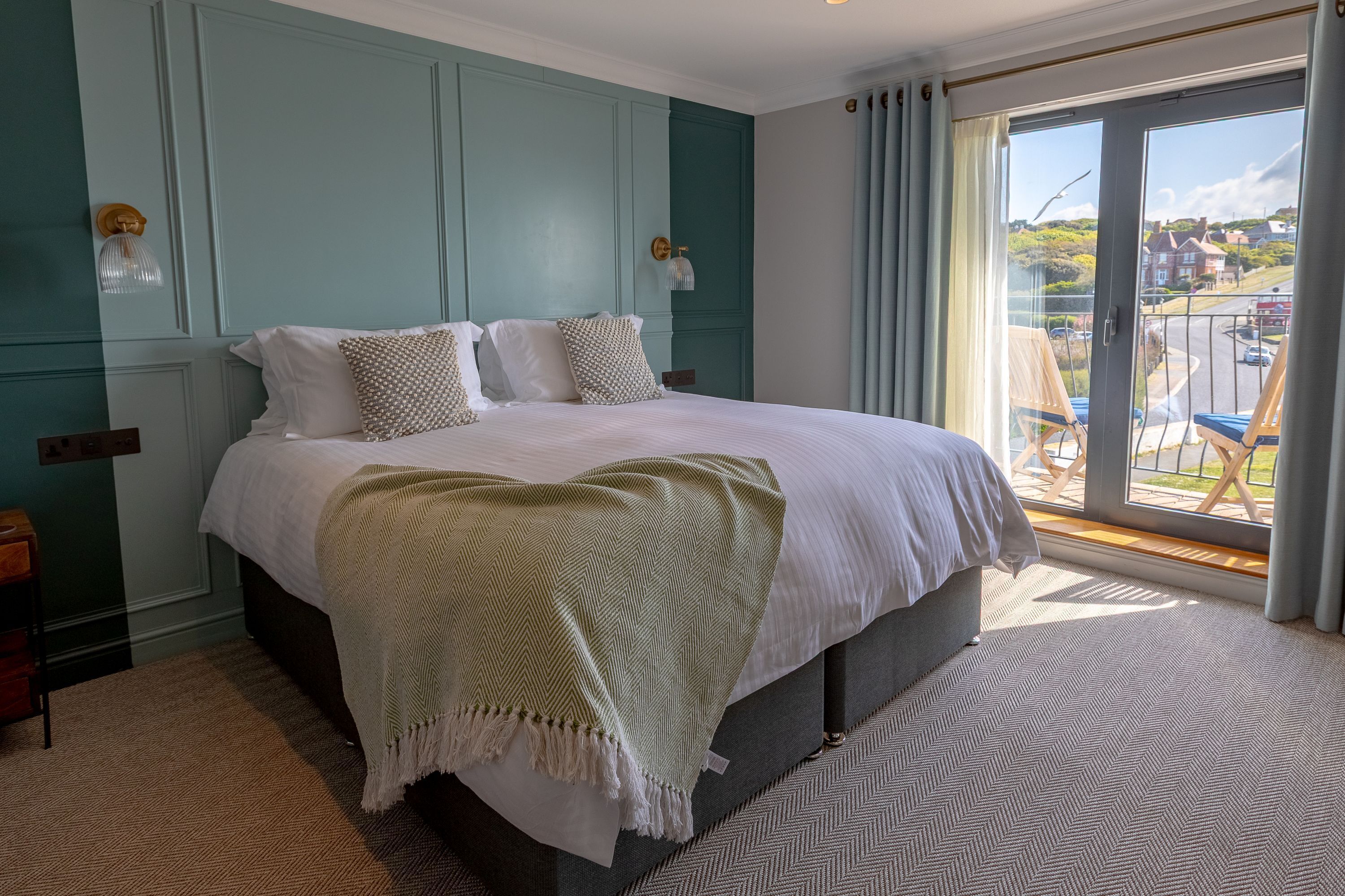 A bedroom with a large bed, a view of the outside, and a balcony with chairs.