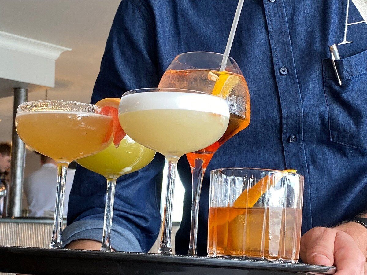 Um bartender segurando uma bandeja com três coquetéis diferentes e um pequeno copo de uísque.