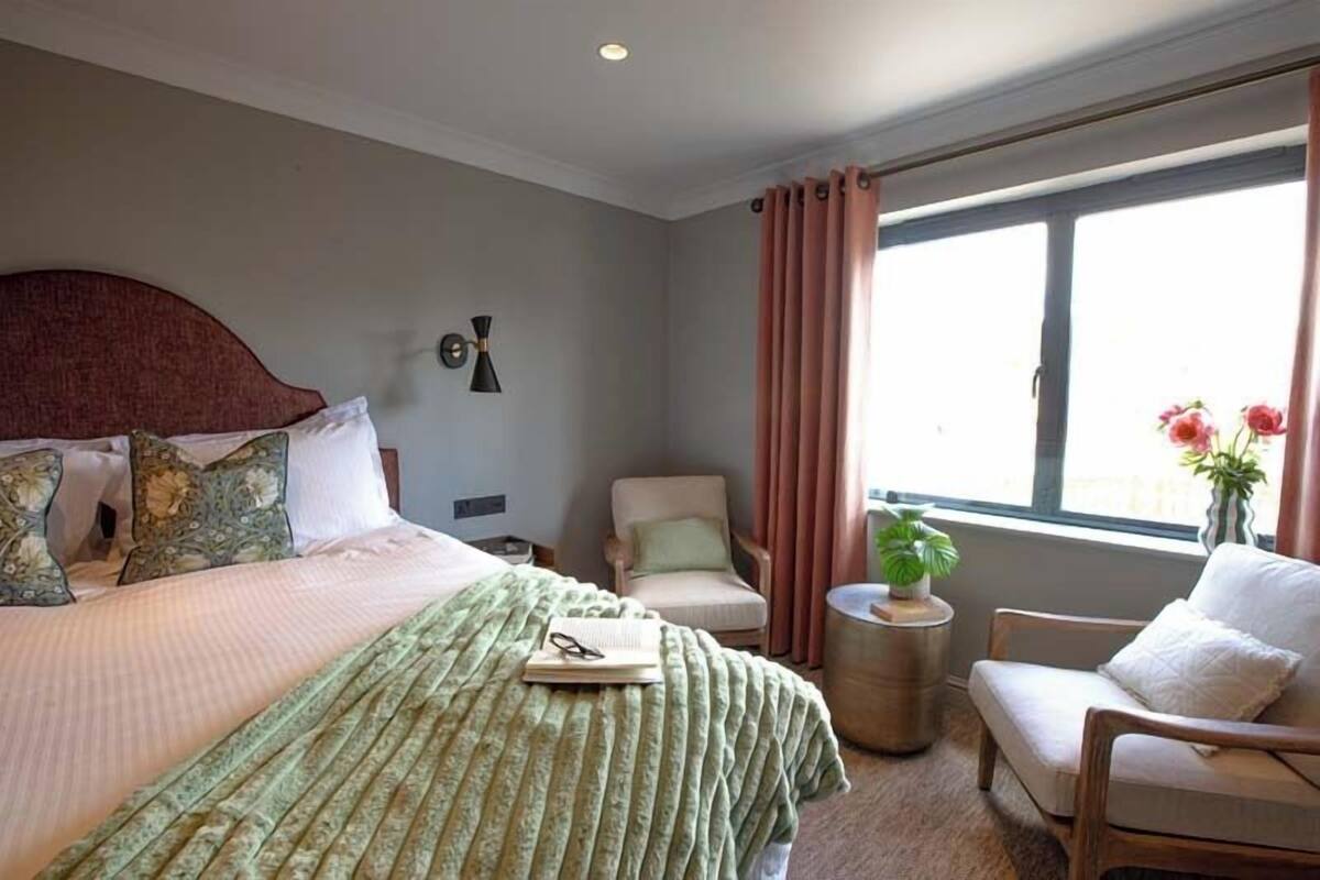 A bedroom with a bed, a chair, a small table, and a window with curtains.