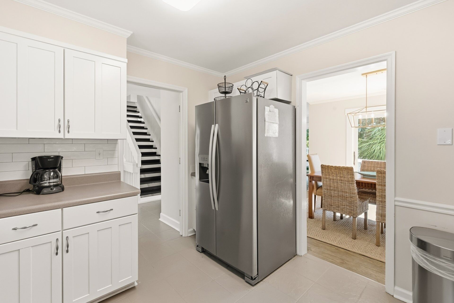 Una cuina moderna amb armaris blancs, un refrigerador d'acer inoxidable i una cafetera al taulell.