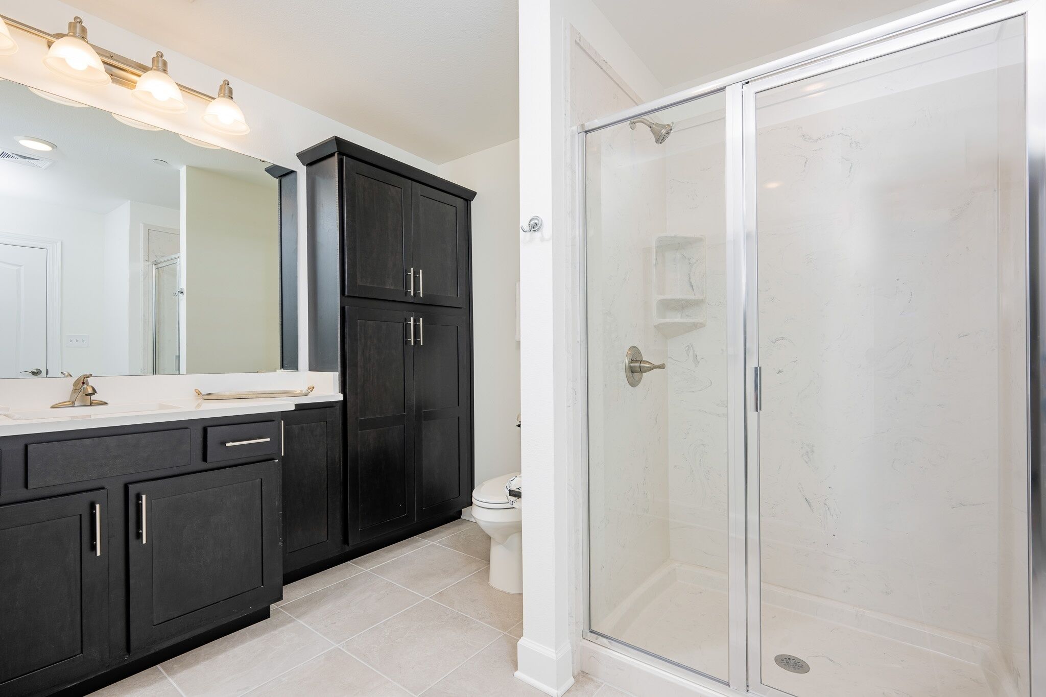 A bathroom with a dark wood vanity, a white toilet, and a glass-enclosed shower.