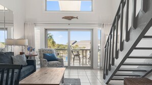 A spacious living area with a wooden coffee table, a sofa, and a patterned armchair. A large fish decoration hangs from the ceiling, and a staircase is visible to the right. - Grandview 2 Bedroom Condo (Miramar Beach)
