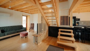 A spacious living area with a wooden staircase, a sofa, a chair, and a kitchen area.