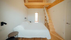 A bedroom with a bed, a small table, and a wooden staircase.