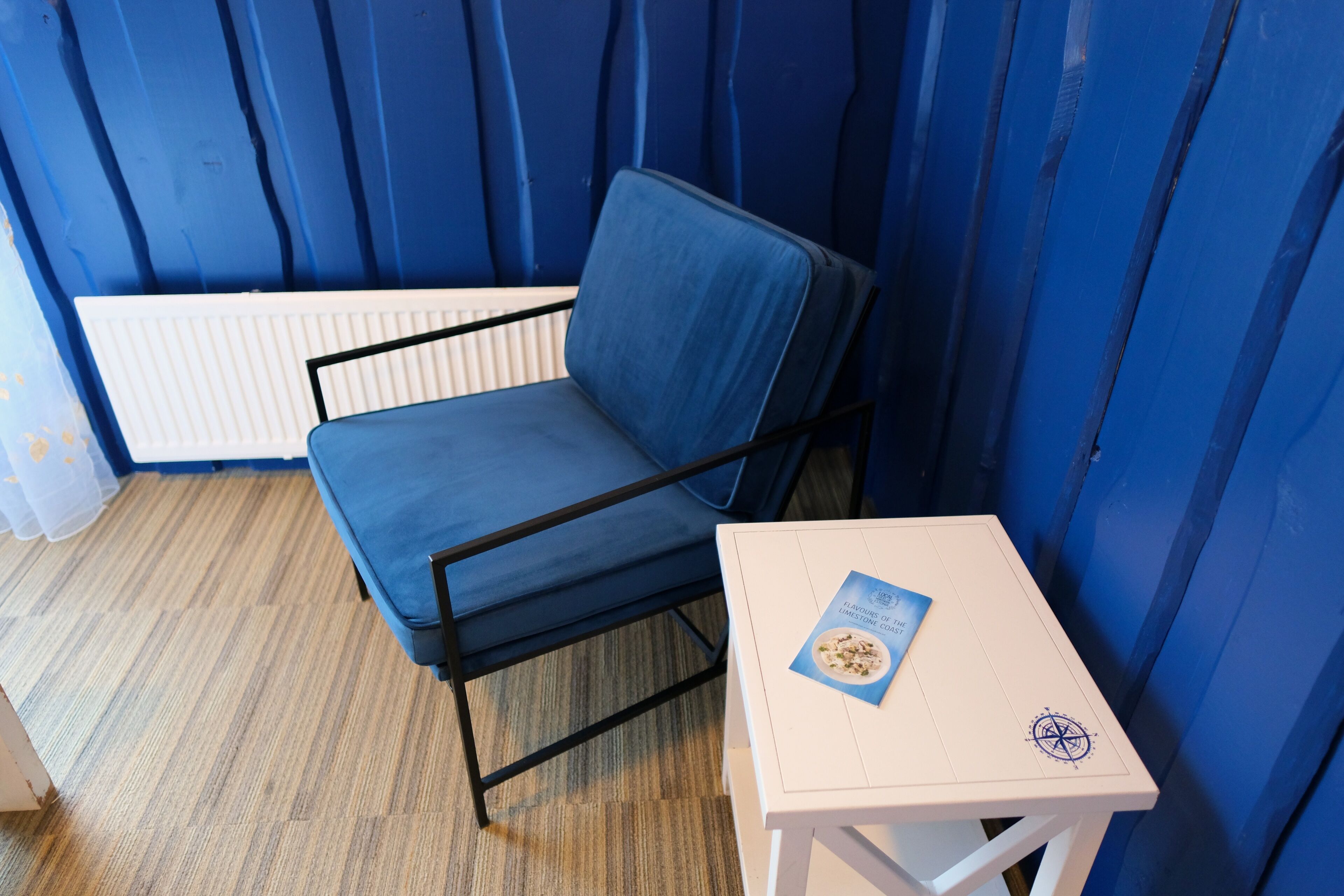 Une chaise bleue, avec une table blanche à côté, le tout placé contre un mur bleu.
