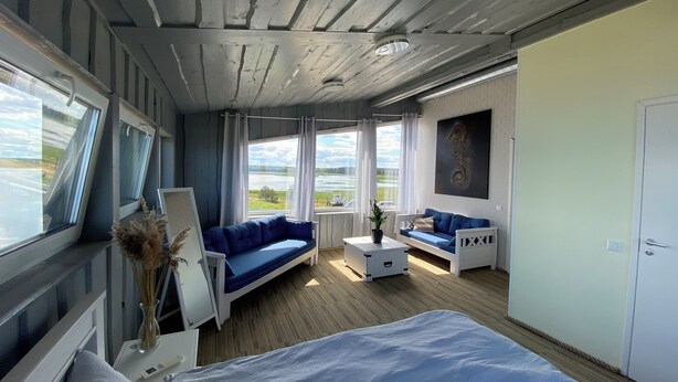 Une pièce comprenant un lit, un canapé bleu, une table basse blanche et une fenêtre donnant sur un lac.
