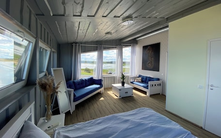 A room with a bed, a blue sofa, a white coffee table, and a window with a view of a lake.