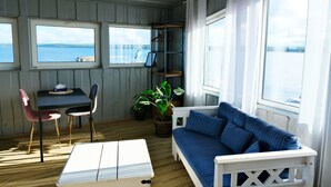 Une pièce avec un canapé blanc, une petite table et deux chaises. Il y a des fenêtres donnant sur la mer.